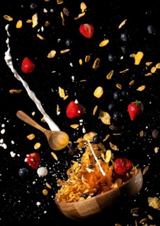 Cornflakes, milk, strawberries and blueberries fly out of a bowl against a black background