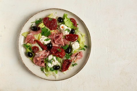 Salad with dried tomatoes, prosciutto, soft cheese, olives, homemade, top view