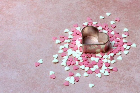 Heart-shaped cookie cutter and sugar hearts on a pink background