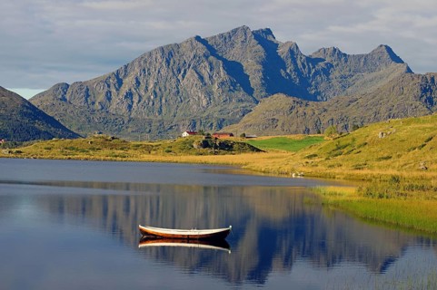 A small wooden boat floats on a calm lake with majestic mountains in the background, Leknes,