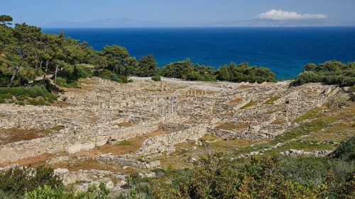 Ruins of an ancient site in front of a blue sea and tree-lined terrain, Kamiros, Archaeological