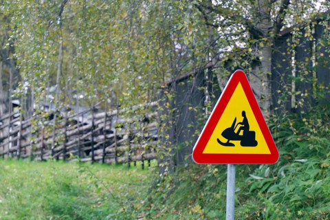 Red and yellow warning sign for tobogganing on a grassy hill in a natural environment with trees,