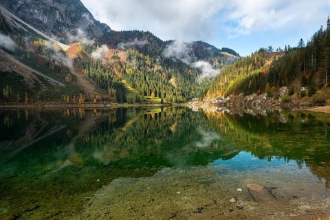 The Vordere Gosausee in autumn with a view of the Gasthof Gosausee. Sun and clouds. Reflection.