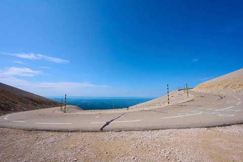 An empty mountain road with a hairpin bend under a clear blue sky and barren landscape, Mont