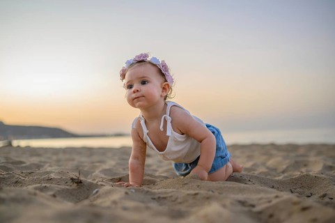 A baby in summer clothes crawls on the beach at sunset