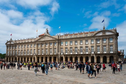 A large baroque stone structure with many windows and visitors in front of it in an open square