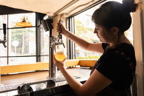 Profile silhouette of a woman serving draft beer in a bar with large windows during the day. The