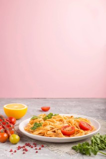 Semolina pasta with tomato pesto sauce, orange and herbs on a white ceramic plate on a gray and