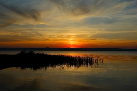 Dramatic sunset at Lake Neusiedl in Austria with colourful orange and red illuminated cloudy sky,