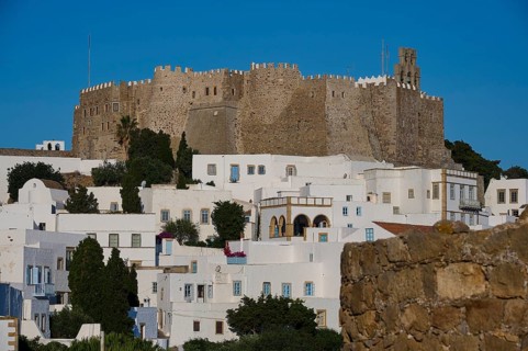 Hill with a castle and traditional white houses surrounded by trees and vegetation under a clear