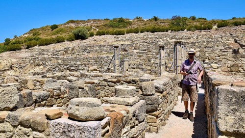 Man exploring an archaeological site with ancient stone ruins under a blue sky, Kamiros,