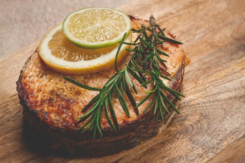 Salmon steak, fried, on a cutting board, top view, rosemary, lemon and lime, homemade, one serving,