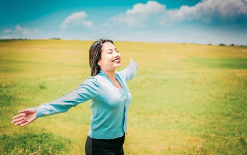 Serene young woman breathing fresh air in beautiful field spreading arms. Happy girl spreading arms