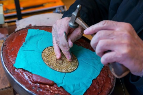 Close-up of hands engraving a detailed pattern on a metal plate in an artisanal process, Toledo,
