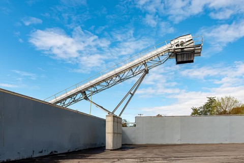 Large conveyor belt towers over a wall, contrasting with blue sky