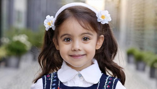 A little girl with a flower headband and dark hair smiles trustingly into the camera, AI generated,