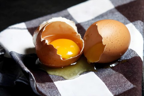 Cracked egg partially spilled on a checkered tablecloth, AI generated