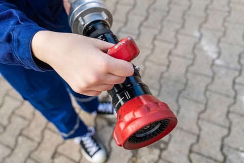 Child holding a fire hose with red handles on a cobbled floor, fire brigade, Enzklösterle, Black