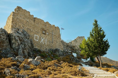 Stone ruin with cross on a hill, stairway and Greek flag under a clear sky, St John's Castle, Oxi