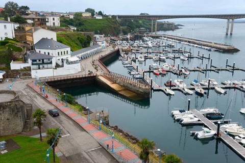 View of a harbour with numerous boats, surrounding architecture and a bridge in the background on a