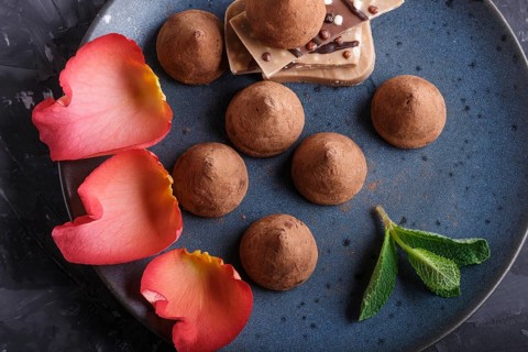 Chocolate truffle on blue ceramic plate on black concrete background decorated with rose petals.