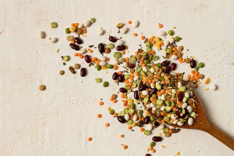 Wooden spoon, with an assortment of legumes, beans, peas, top view, on a light background