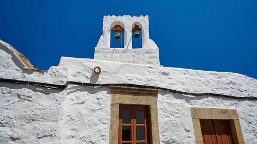 White building with bell tower and windows in front of a bright blue sky, Chora, Old Town, Patmos,