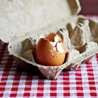 Cracked egg partially spilled on a checkered tablecloth, AI generated