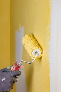 Wall is painted with yellow paint, hand with paint roller