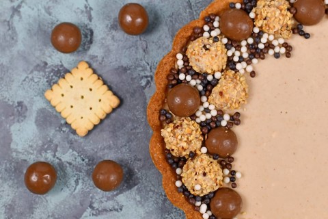 Close up of of sweet tart with cheesecake milk chocolate cream filling topped with pralines and