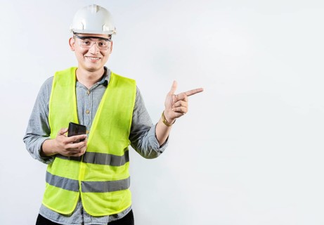 Smiling engineer holding cell phone and pointing an advertisement. Young latin engineer holding