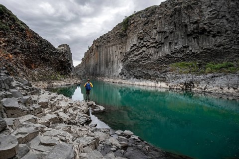 Tourist standing by the river in Stuðlagil Canyon, turquoise blue river between basalt columns,