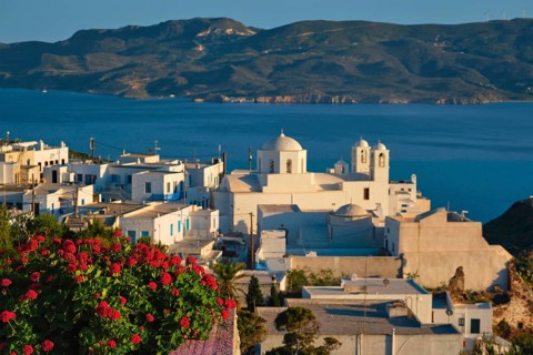 View of Plaka village on Milos island over red geranium flowers on sunset. Plaka town, Milos