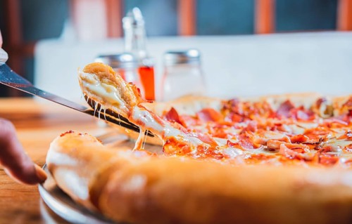 Homemade ham and cheese pizza with spatula on table. Hand taking a slice of ham pizza with the