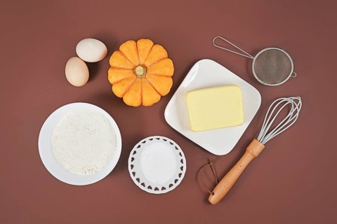 Pumpkin pie ingredients and baking tools on brown background