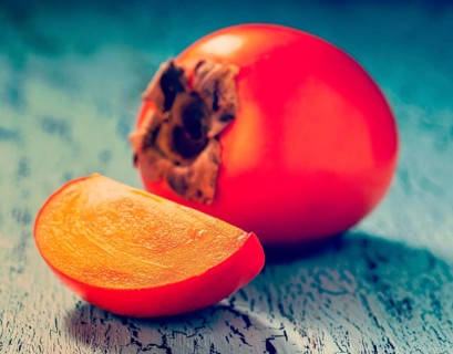 Vintage retro effect filtered hipster style image of fresh ripe persimmon with slice on a blue