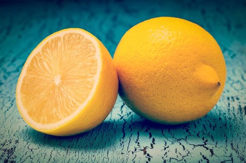 Vintage retro effect filtered hipster style image of lemon and cut half slice on blue wooden