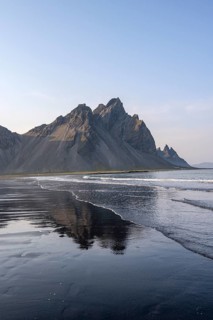 Black lava beach, sandy beach and sea, mountains Klifatindur reflected in the water, Eystrahorn and