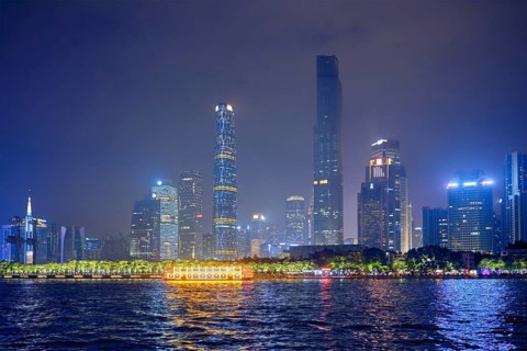 Guangzhou cityscape skyline over the Pearl River with tourist boat illuminated in the evening.
