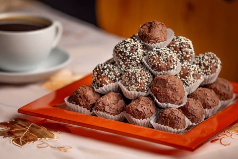 Close-up of rum balls with chocolate on a plate and a coffee cup in the background