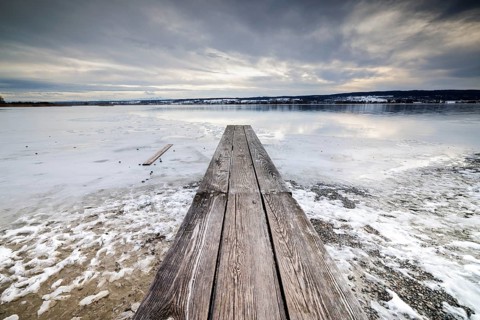 Frozen lake with wooden dock leading to the horizon, under a grey sky, campsite, Hegne, Lake