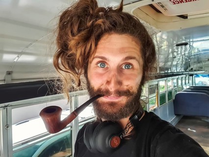 Close up portrait shot of a curious looking young man with long hair, big headphones and a wooden