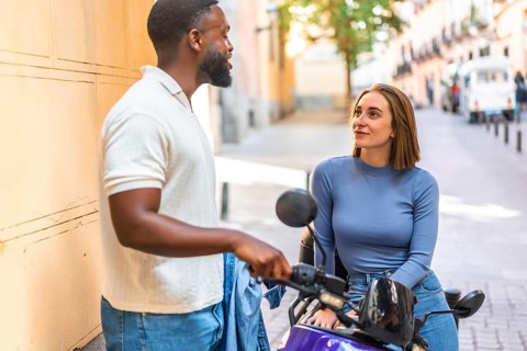 African man talking with a caucasian woman sitting on scooter motorbike parked in the street