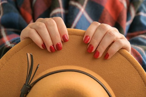 Stylish red female nails. Woman in poncho holding brown trendy hat. Modern Beautiful manicure.