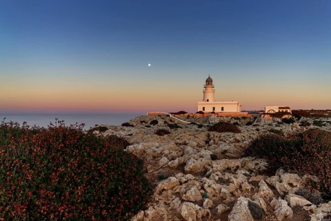 A view of the Cap de Cavalleria Lighthouse on Menorca at sunset with a full moon rising