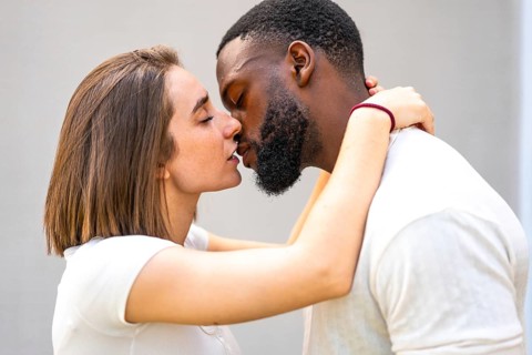 Side view close-up of a tender multi-ethnic couple with white clothes kissing and embracing