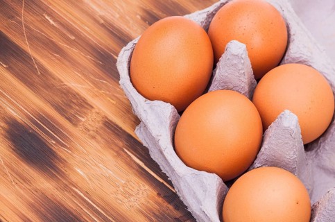 Image shows some raw eggs in a box on a wooden plate