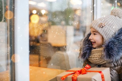 Portrait of joyful girl with a gift box for Christmas near the glass shop window in winter with