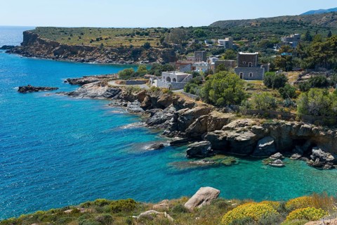 Coastal landscape with rocky shores, clear blue water and picturesque houses under a clear sky,