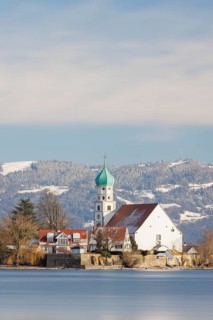 St George's Church with green tower in front of snow-covered Pfänder, surrounded by village houses,